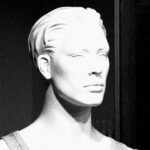 Close-up of a monochrome mannequin head with dramatic lighting and shadows.